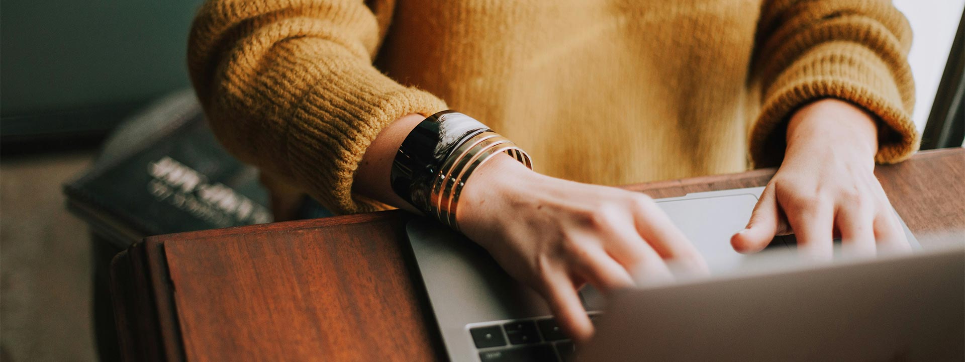 A person wearing a yellow jumper types on a laptop.