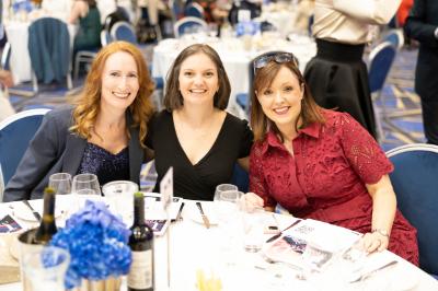 Three women seated together at the MGA Gala Dinner 2025 smiling at the camera