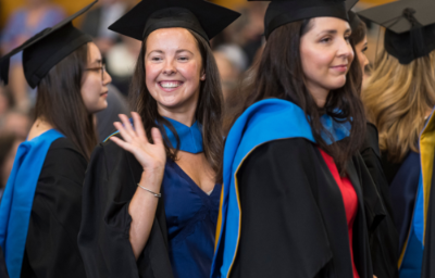 Student with conferring hat and gown waving in queue at graduation