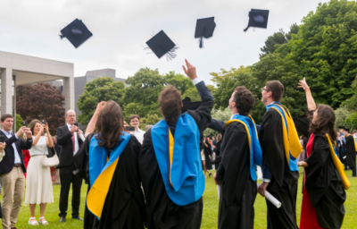 Students in conferring gowns throwing hats in the air outside O Reilly Hall