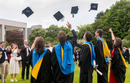 Students in conferring gowns throwing hats in the air outside O Reilly Hall