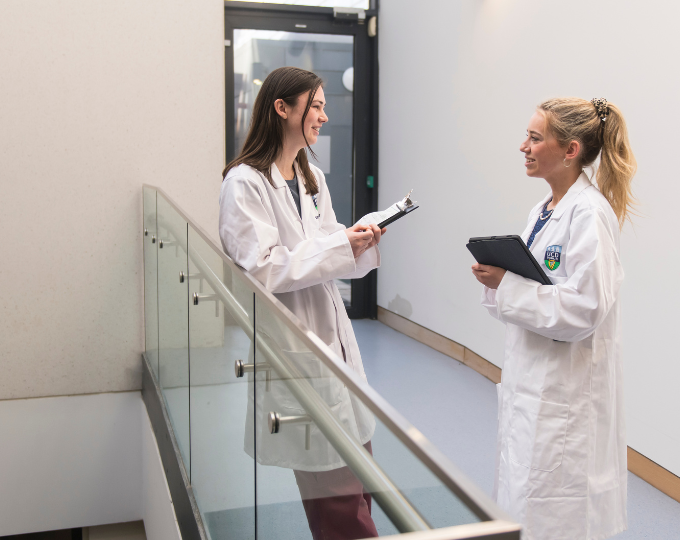 two students in white coats in the health sciences building