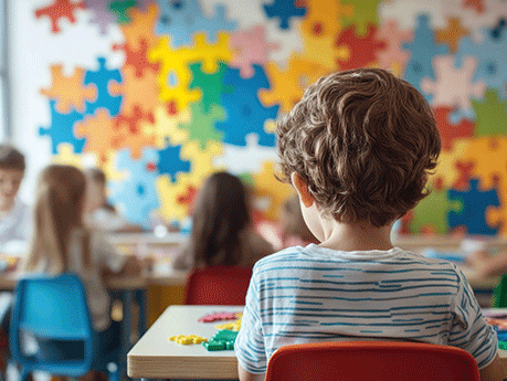 Children are sitting at their desks in a preschool classroom in a kindergarten decorated with multicolored jigsaw puzzles. World Autism Awareness Day.