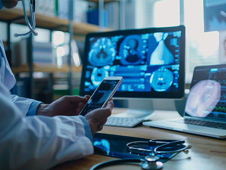 A male doctor in a white coat analyzes medical data on a smartphone while reviewing scan images on multiple computer screens in a bright office.