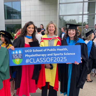 Academic with two graduates holding a Class of 2025 sign at UCD
