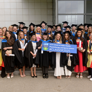 UCD graduate class in caps and gowns holding a sign saying Class of 2025