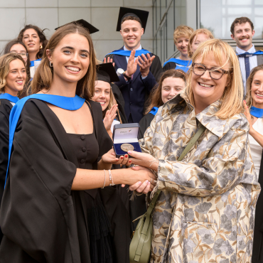 UCD graduate receiving a medal in front of class of graduates