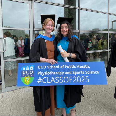 Two graduates in caps and gowns holding a sign saying Class of 2025