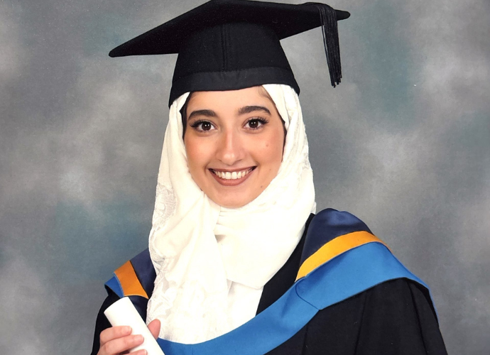 A female graduate wearing a gradation cap and gown and holding a scroll